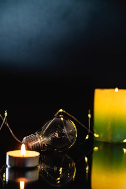 Ampuller ve yanan bir mum siyah bir arka planda. Aynı zamanda çelenk, bokeh. bayram karartması konsepti