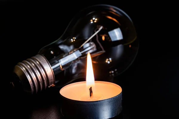 Electric lamp and candle on a dark background. Incandescent lamp and candle. No or power outage. High electricity prices. Saving electricity.