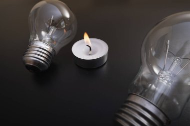 Electric lamp and candle on a dark background.  Incandescent bulb and candle. Power cut or power outage. High electricity prices. Saving electricity. Symbol of return to the past.