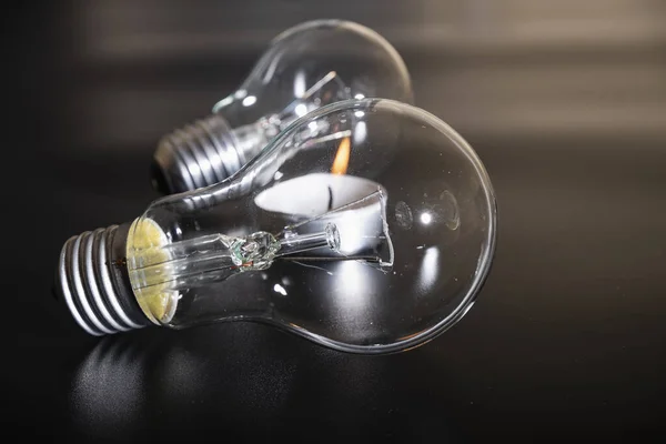 Electric lamp and candle on a dark background.  Incandescent bulb and candle. Power cut or power outage. High electricity prices. Saving electricity. Symbol of return to the past.
