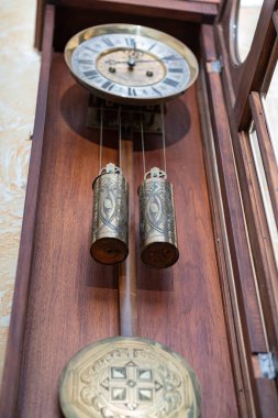 Old wooden clock with a pendulum hanging on the wall