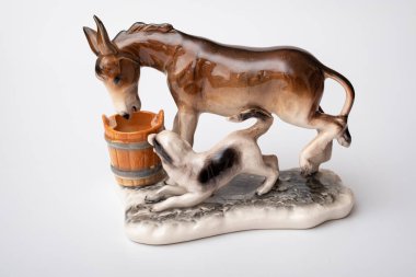 figurine of a donkey that drinks water and next to it a dog teases a donkey