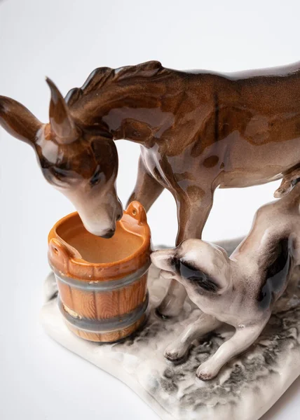 figurine of a donkey that drinks water and next to it a dog teases a donkey