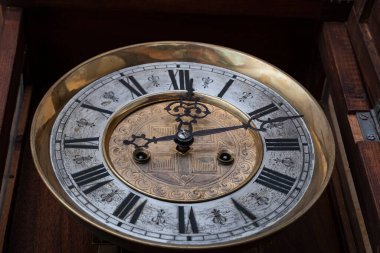 Old wooden clock with a pendulum hanging on the wall