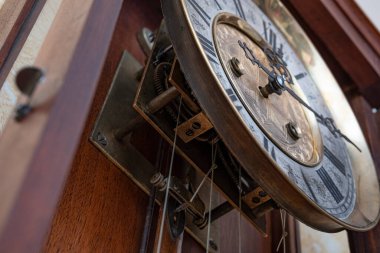 Old wooden clock with a pendulum hanging on the wall