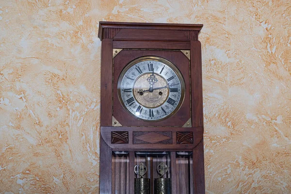 Old wooden clock with a pendulum hanging on the wall
