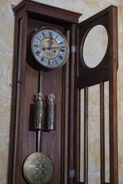 Old wooden clock with a pendulum hanging on the wall