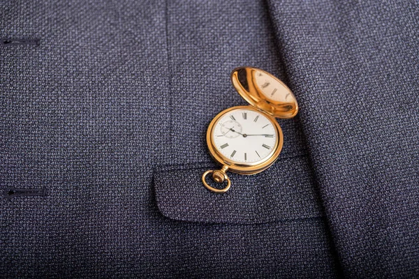 Golden pocket watch on the background of a man\'s suit. Retro style and vintage fashion.