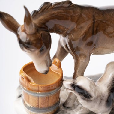 figurine of a donkey that drinks water and next to it a dog teases a donkey
