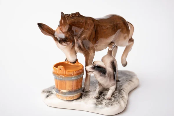 figurine of a donkey that drinks water and next to it a dog teases a donkey