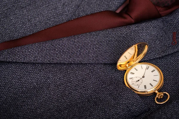 Golden pocket watch on the background of a man\'s suit. Retro style and vintage fashion.