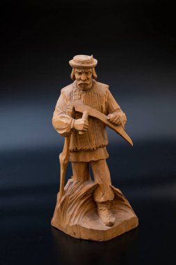 Siyah arka planda el yapımı ahşap bir heykel. Büyükbaba samanlıkta tırpanla geziyor.