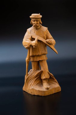 Siyah arka planda el yapımı ahşap bir heykel. Büyükbaba samanlıkta tırpanla geziyor.