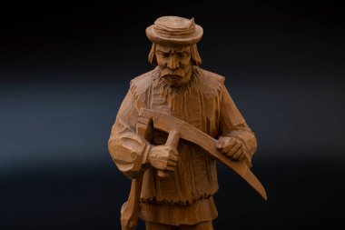 Siyah arka planda el yapımı ahşap bir heykel. Büyükbaba samanlıkta tırpanla geziyor.