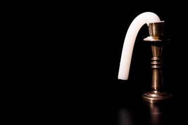 Güneşte duran eğri bir mum. Siyah arkaplanda bir şamdanı kesmek.