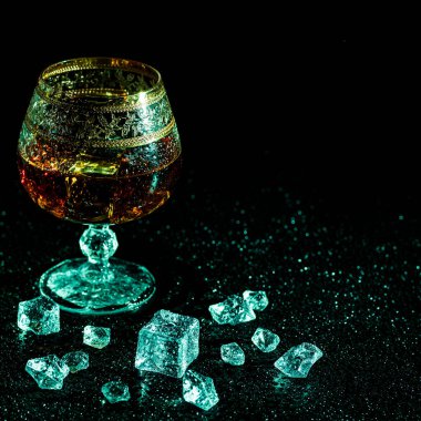Koyu arkaplanda konyak ve buzlu bir bardak. Alkolizm ve içki kavramı