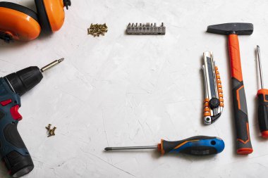 Çalışma araçları, çekiç, tornavida, pense, elektrikli matkap, mezura, beyaz arka planda vidalar üst görünüm.