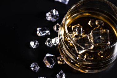 Koyu arkaplanda konyak ve buzlu bir bardak. Alkolizm ve içki kavramı