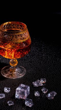 Koyu arkaplanda konyak ve buzlu bir bardak. Alkolizm ve içki kavramı