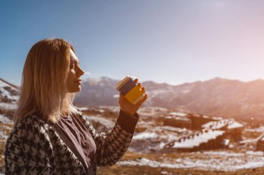 blonde woman drinking hot tea in mountains