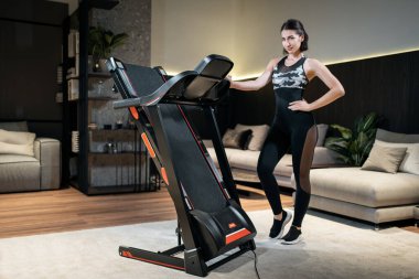 Atletik kadın evinde koşu bandı monte ediyor.