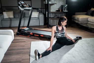 Güzel bir kadın esneyip koşu bandında antrenmana hazırlanıyor.