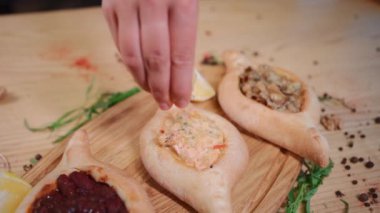 closeup of hand adding lemon on khachapuri boat with fish on wooden board