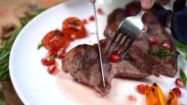 eating roasted meat steak with fork and rosemary or tomato on white plate