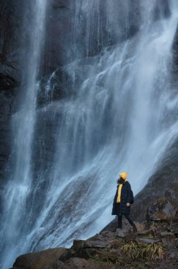 Gürcistan 'da su kenarında duran kabarık ceketli ve sarı örgü şapkalı genç kız seyahat konsepti