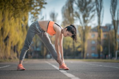Güzel kıvırcık kadın gün batımında açık hava antrenmanından önce ısınıyor.