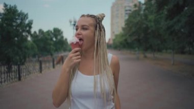 Afro örgülü genç bir kadın dışarıda dondurma yiyor.