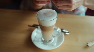 Kadın kişi kafede latte ya da cappuccino içer ve şekerle samanı karıştırır. Yüksek kaliteli FullHD görüntüler