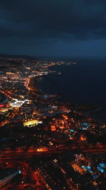 Okyanus kıyısında, Tenerife, Kanarya Adası 'nda güzel aydınlatılmış gece şehri hava manzarası. Yüksek kalite 4k görüntü, hava aracı, makara ve hikayeler için dikey