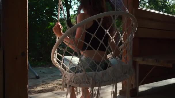 Arka Planda Oturan Örgü Örülmüş Hamak Sandalyesinde Sallanan Bir Kız — Stok video