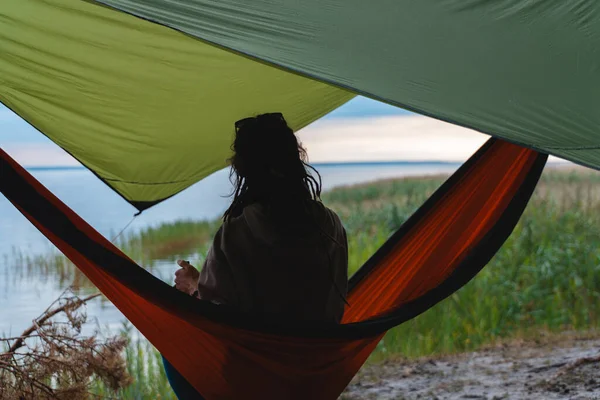 Rastgele saç stili olan hippi bir kadının arka planda doğada hamakta yatması, doğada dinlenmesi. Yüksek kalite fotoğraf