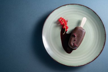 Çubuklu çikolatalı dondurma ve siyah arka planda kırmızı frenk üzümü ile süslenmiş meyve.