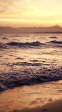 Deniz sahilinde güzel bir gün batımı, mavi sakin su dalgaları, huzur verici dalgalarla okyanus kıyıları, tatil konsepti. Yüksek kalite 4k görüntü, dikey video