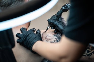 Profesyonel kadın sanatçı erkek elinde Japon şeytan maskesinin stil sahibi siyah dövmesini yapıyor kuaförde iğne ve makine ile, omuz vücut sanatı. Yüksek kalite fotoğraf