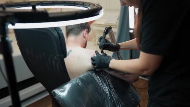 Profesyonel kadın sanatçı erkek elinde Japon şeytan maskesinin stil sahibi siyah dövmesini yapıyor kuaförde iğne ve makina ile, omuz gövdesi 4K. Yüksek kalite 4k görüntü