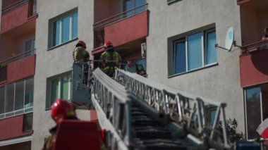 Genişletilmiş merdivenli itfaiye aracı, koruma ekipmanlı itfaiyecilerin acil durum müdahalesi için balkonda çalıştıkları meskun binaya ulaşıyor. Yüksek kalite 4k görüntü