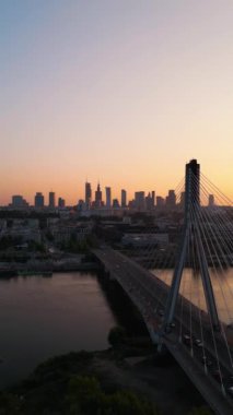 Günbatımında Vistula nehri üzerinde modern kablo köprüsü olan Varşova şehrinin ufuk çizgisi, arka planda modern gökdelenler, hava manzarası. Yüksek kalite 4k görüntü, dikey video