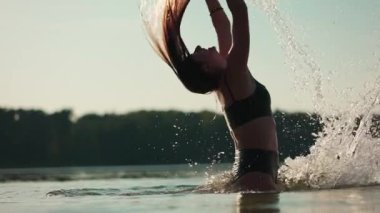 Genç seksi kadın plajda dinleniyor, yüzüyor ve mavi deniz suyuyla oynuyor, uzun saçlarıyla sıçramalar yapıyor, yaz tatili konsepti, yavaş çekim. Yüksek kaliteli FullHD görüntüler