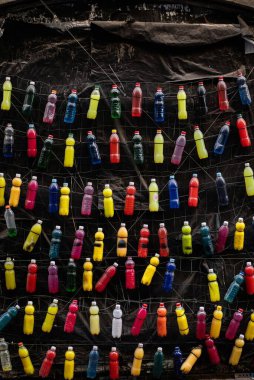 Düzenli bir düzende çeşitli renklere sahip çok sayıda içecek şişesi koyu bir arkaplanda asılı duruyor..
