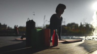 Gün batımında yoga yapan genç, güzel bir kadın. Vücut bilinci açık olan, köpük silindirli, bloklu, kokulu Hint sopalı ve diğer aksesuarlarla egzersiz yapan biri. Yüksek kalite 4k görüntü