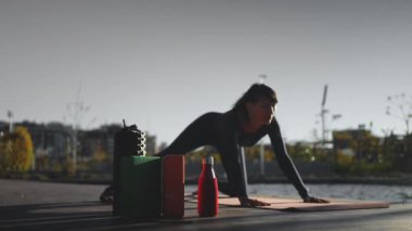 Gün batımında yoga yapan genç, güzel bir kadın. Vücut bilinci açık olan, köpük silindirli, bloklu, kokulu Hint sopalı ve diğer aksesuarlarla egzersiz yapan biri. Yüksek kalite 4k görüntü