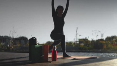 Gün batımında yoga yapan genç, güzel bir kadın. Vücut bilinci açık olan, köpük silindirli, bloklu, kokulu Hint sopalı ve diğer aksesuarlarla egzersiz yapan biri. Yüksek kalite 4k görüntü