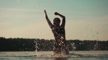 Mutlu kadın gölde ya da nehirde yüzüyor ve oynuyor, zıplıyor, su damlatıyor ve dalgalar yaratıyor, neşeli duygusal kız deniz doğasında tatilden keyif alıyor, ağır çekimde. Merkez FullHD görüntüleri
