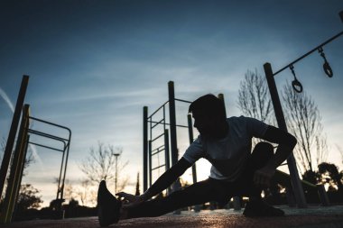 Genç atletik adam spor salonunda egzersiz yapıyor ve gün batımında sokak spor salonunda bacaklarını esnetiyor, vücut geliştirme ve dayanıklılık eğitimi kavramı. Yüksek kalite fotoğraf