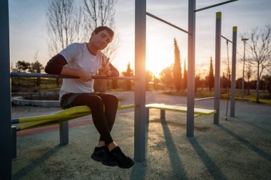 Genç atletik adam gün batımında spor salonunda vücut geliştirme ve dayanıklılık antrenmanı konseptinden sonra gevşemek için spor salonunda kas egzersizi yaptıktan sonra dinleniyor. Yüksek kalite fotoğraf