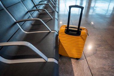 Portatif ve şık sarı bavullar boş havaalanı koltuklarının yanında dinlenirken, gezginler yoğun terminalde, seyahat ve tatil konseptinde bagajlar bekliyor. Yüksek kalite fotoğraf